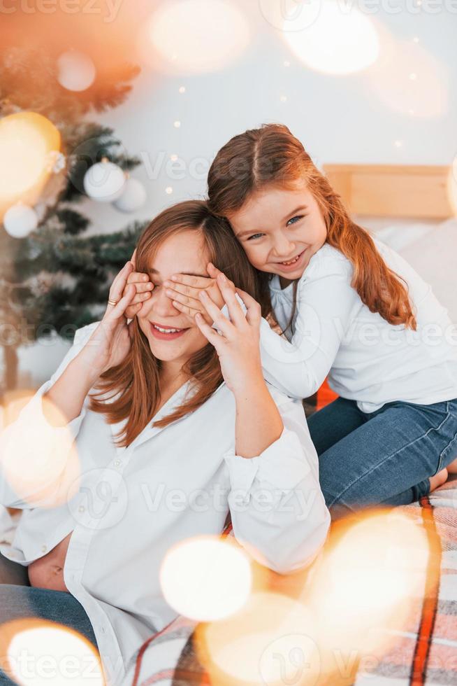 madre con sua poco figlia è avendo divertimento in casa su il letto foto