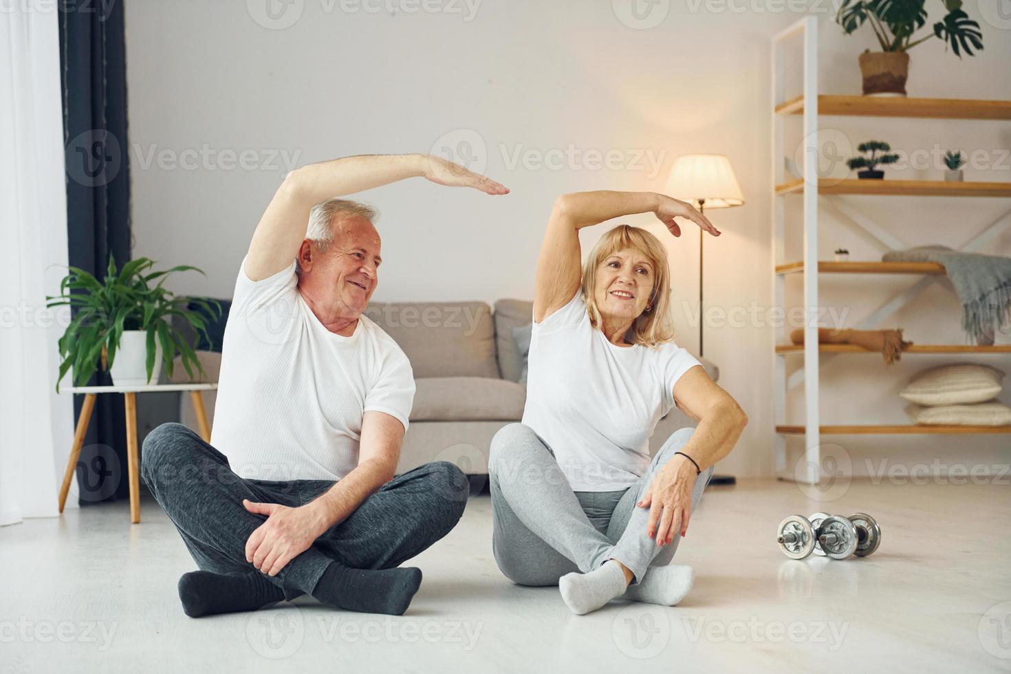 seduta e fare esercizi. anziano uomo e donna è insieme a casa foto