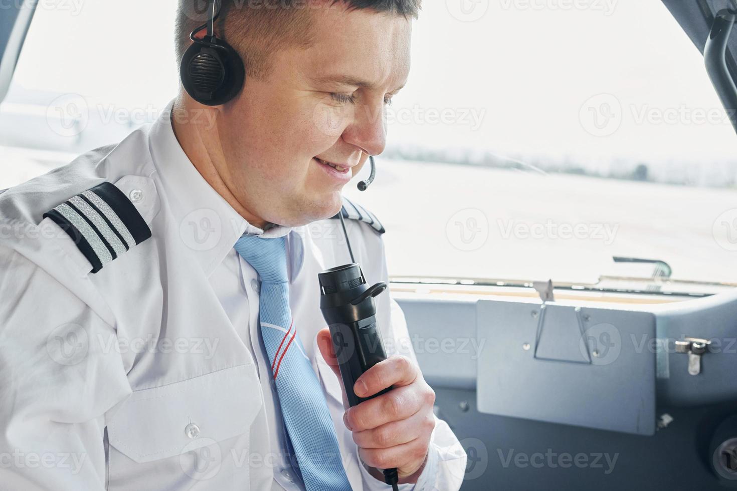 parla per un' microfono. pilota nel formale indossare si siede nel il cabina di pilotaggio e controlli aereo foto
