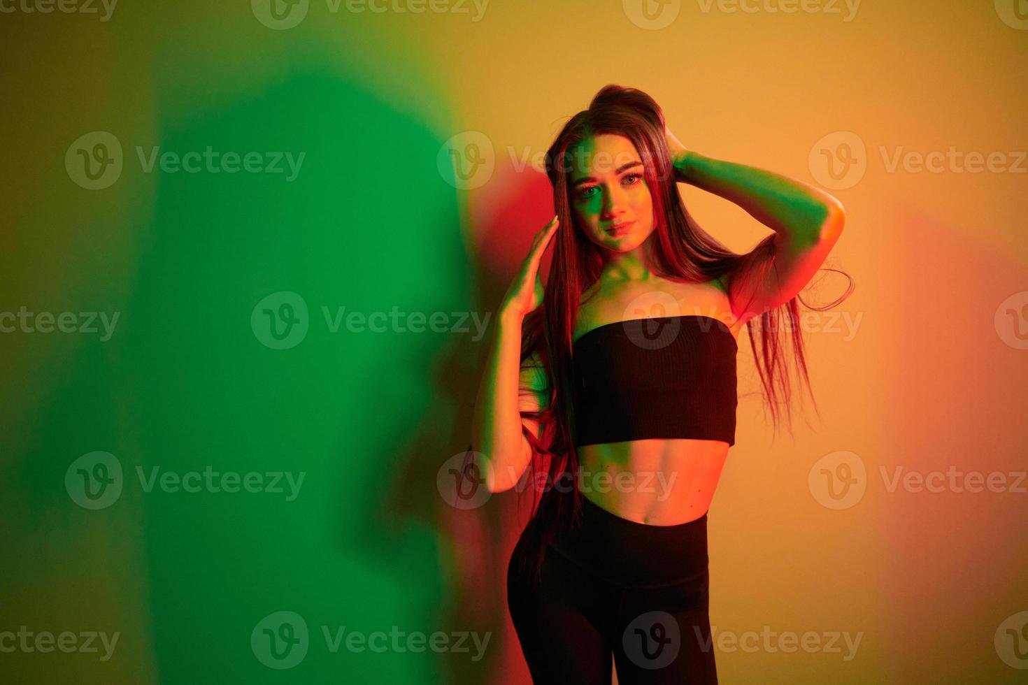 contro parete. alla moda giovane donna in piedi nel il studio con neon leggero foto