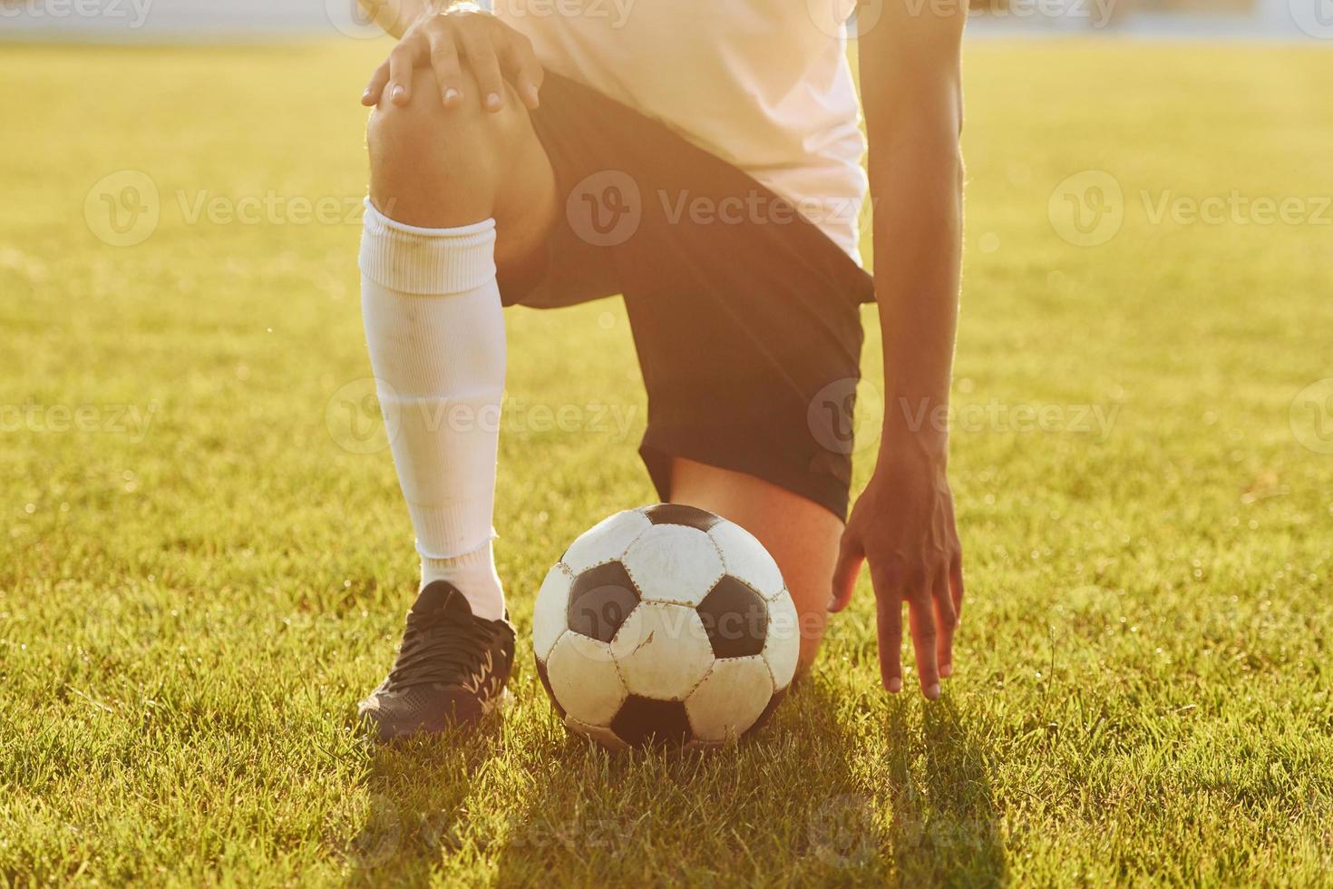 si siede su il ginocchio con sfera. giovane calcio giocatore avere formazione su il allegro campo foto