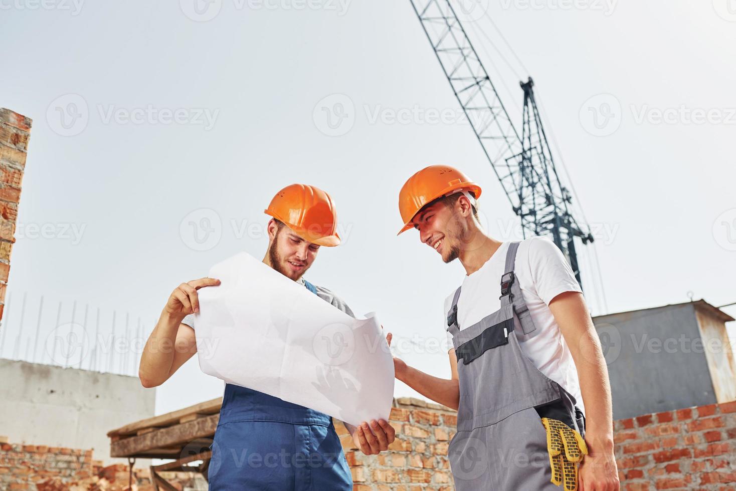 lettura Piano. Due giovane costruzione lavoratori nel uniformi è occupato a il incompiuto edificio foto