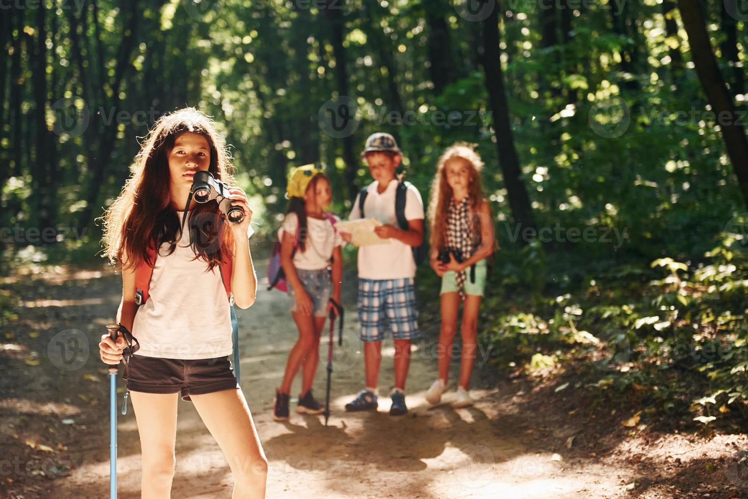 ragazza in piedi nel davanti di sua gli amici. bambini passeggiando nel il foresta con viaggio attrezzatura foto