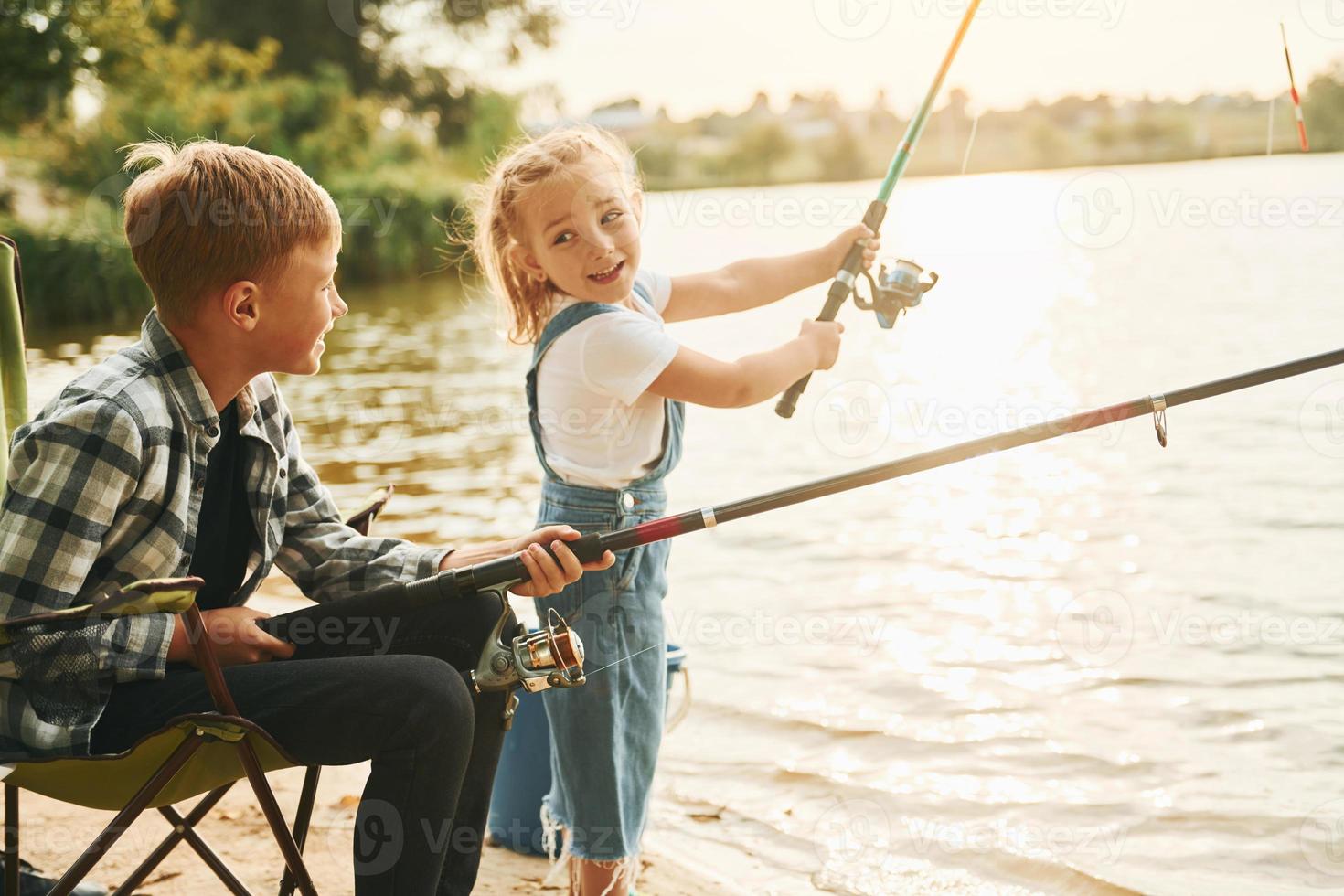medio dimensioni lago. ragazzo con il suo sorella nel su pesca all'aperto a estate insieme foto