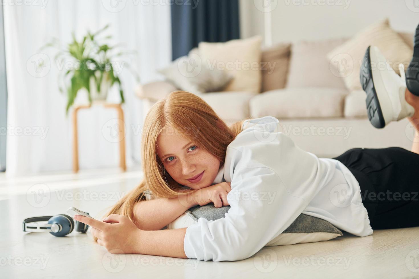 posa giù su il pavimento. femmina adolescente con bionda capelli è a casa a giorno foto