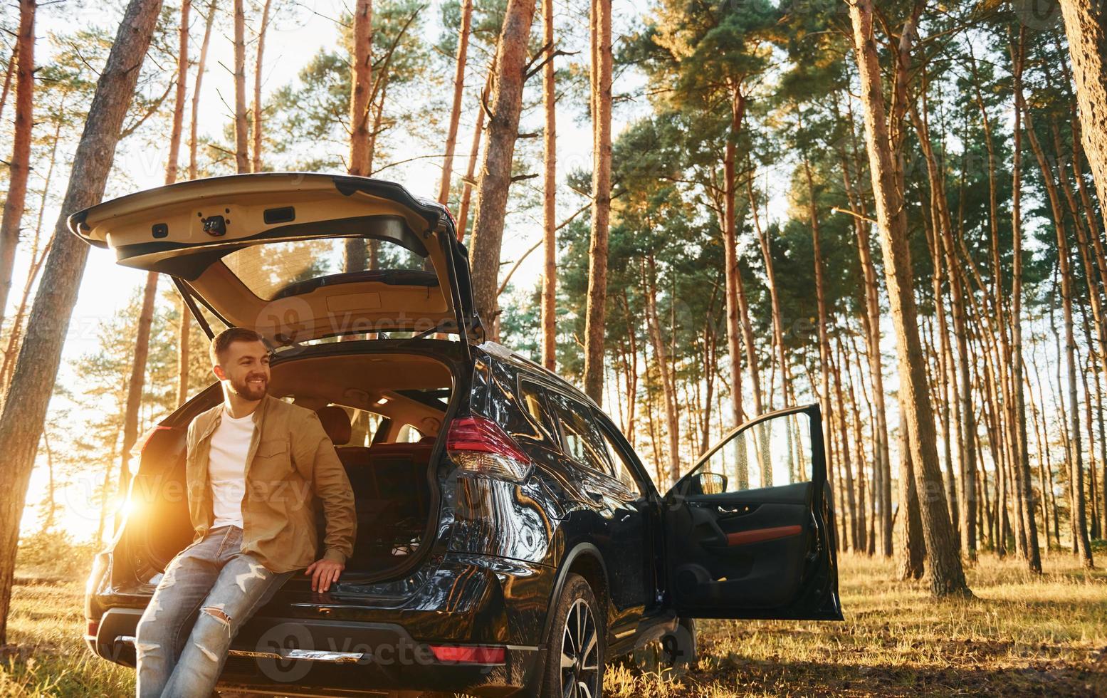 con il suo macchina. uomo nel jeans è all'aperto nel il foresta con il suo nero colorato automobile foto