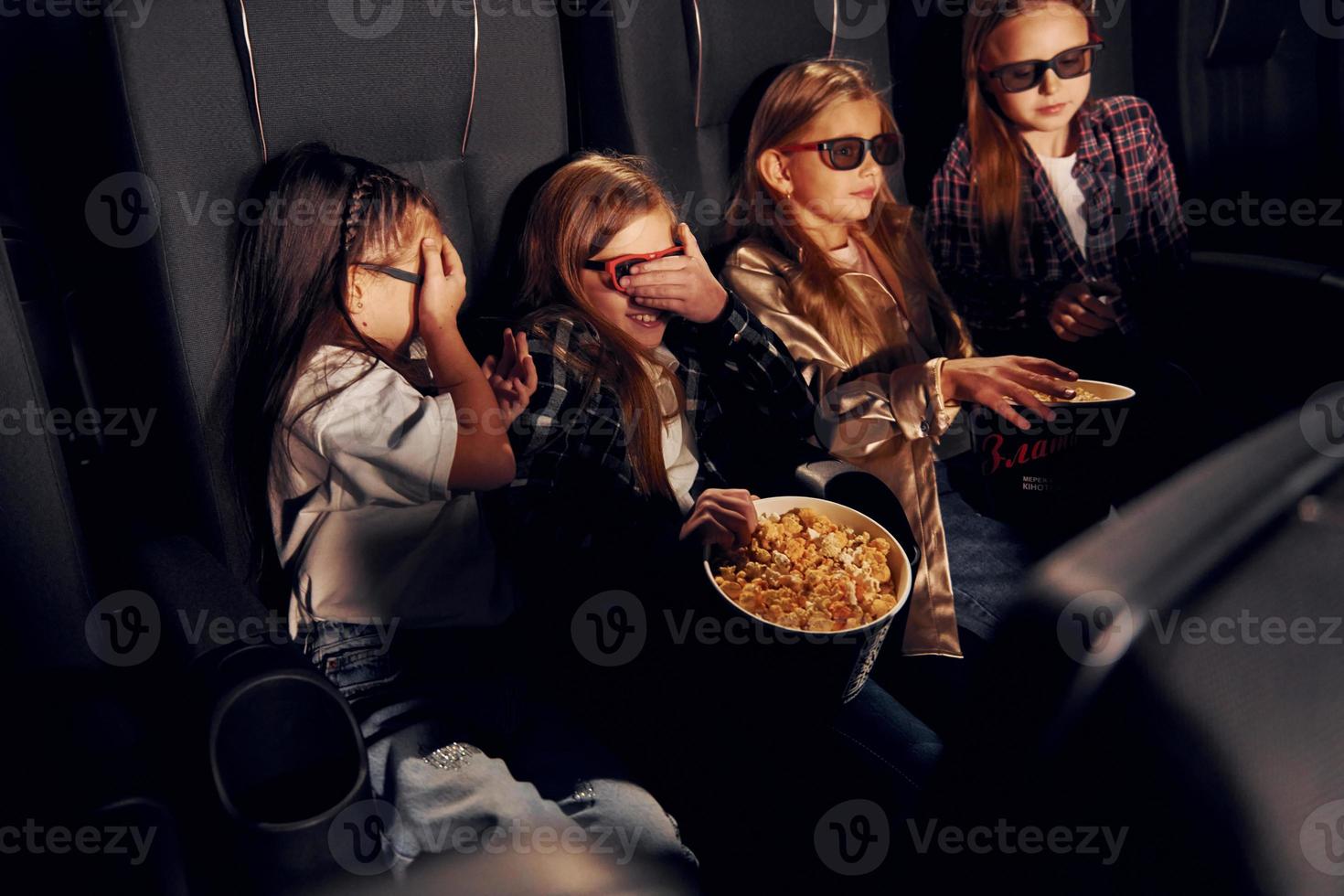 avendo divertimento. gruppo di bambini seduta nel cinema e Guardando film insieme foto