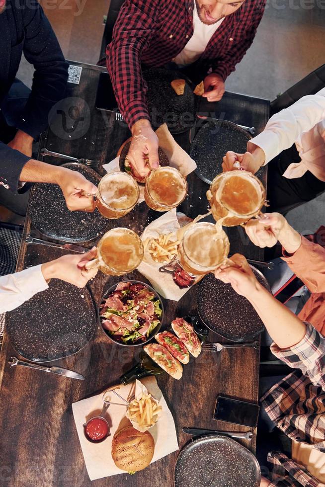 allegro emozioni. gruppo di giovane amici seduta insieme nel bar con birra foto