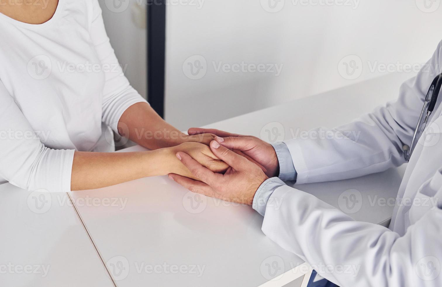 Tenere cliente di il mani. professionale medico nel bianca cappotto è nel il clinica foto