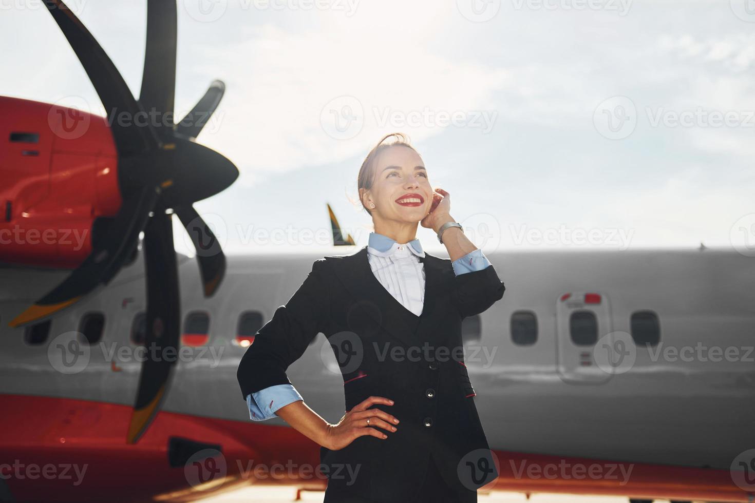 a giorno. giovane hostess quello è nel formale nero Abiti è in piedi all'aperto vicino aereo foto