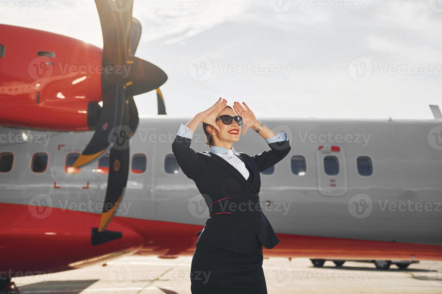 guardare lontano lontano. giovane hostess quello è nel formale nero Abiti è in piedi all'aperto vicino aereo foto