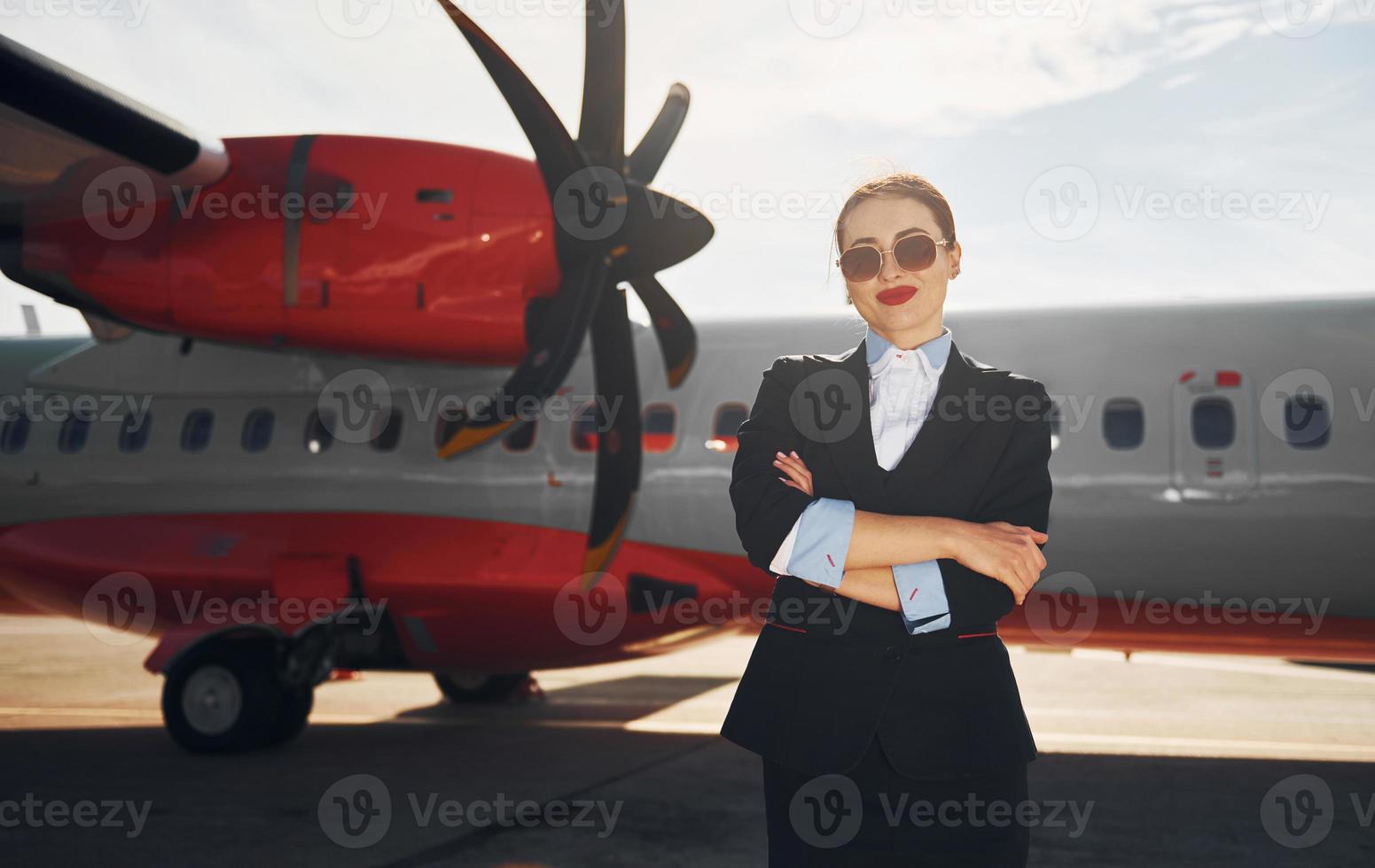 giovane hostess quello è nel formale nero Abiti è in piedi all'aperto vicino aereo foto