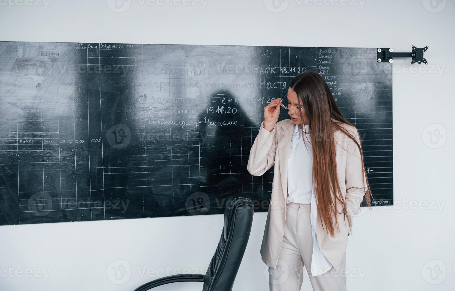 giovane inteligente donna con bicchieri in piedi vicino lavagna foto