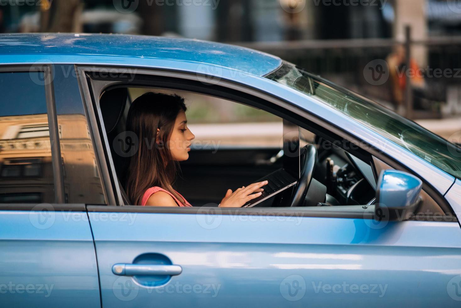 giovane donna utilizzando il computer portatile nel sua auto mentre guida. foto