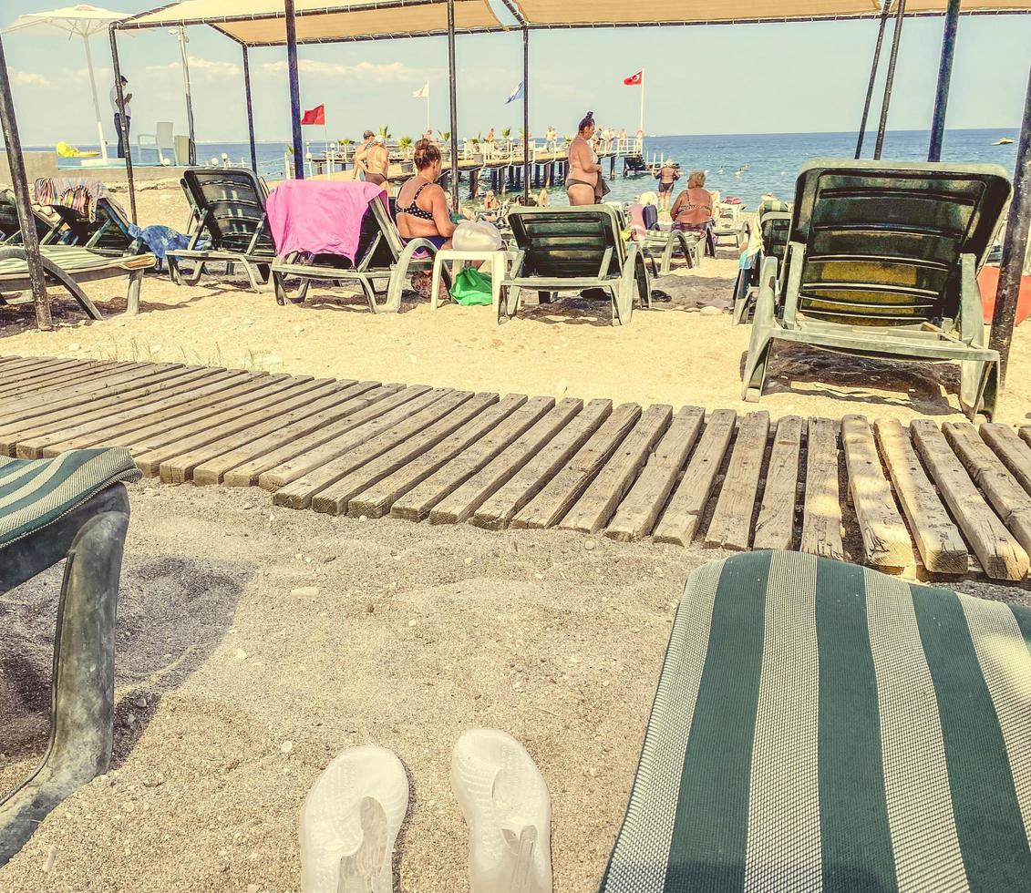 spiaggia per turisti. sabbioso terra, verde tessuto letti. su il sabbia - un' pontone fatto di di legno bastoni. vicino il lettini Là siamo gomma da cancellare pantofole di turisti foto