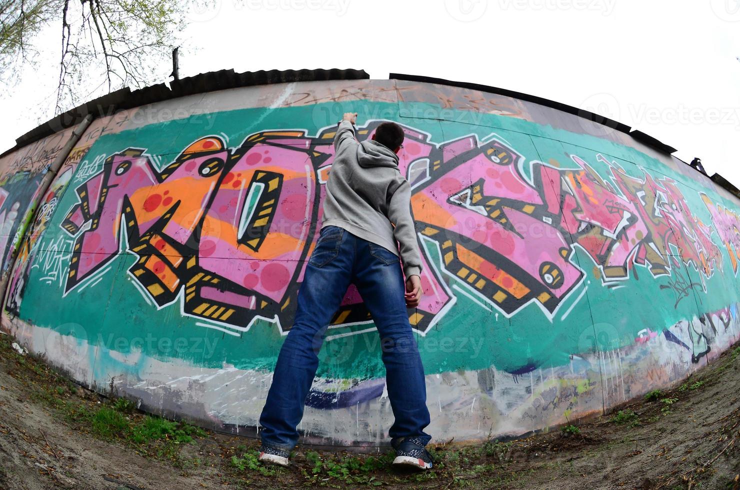 un' giovane tipo nel un' grigio felpa con cappuccio vernici graffiti nel rosa e verde c foto