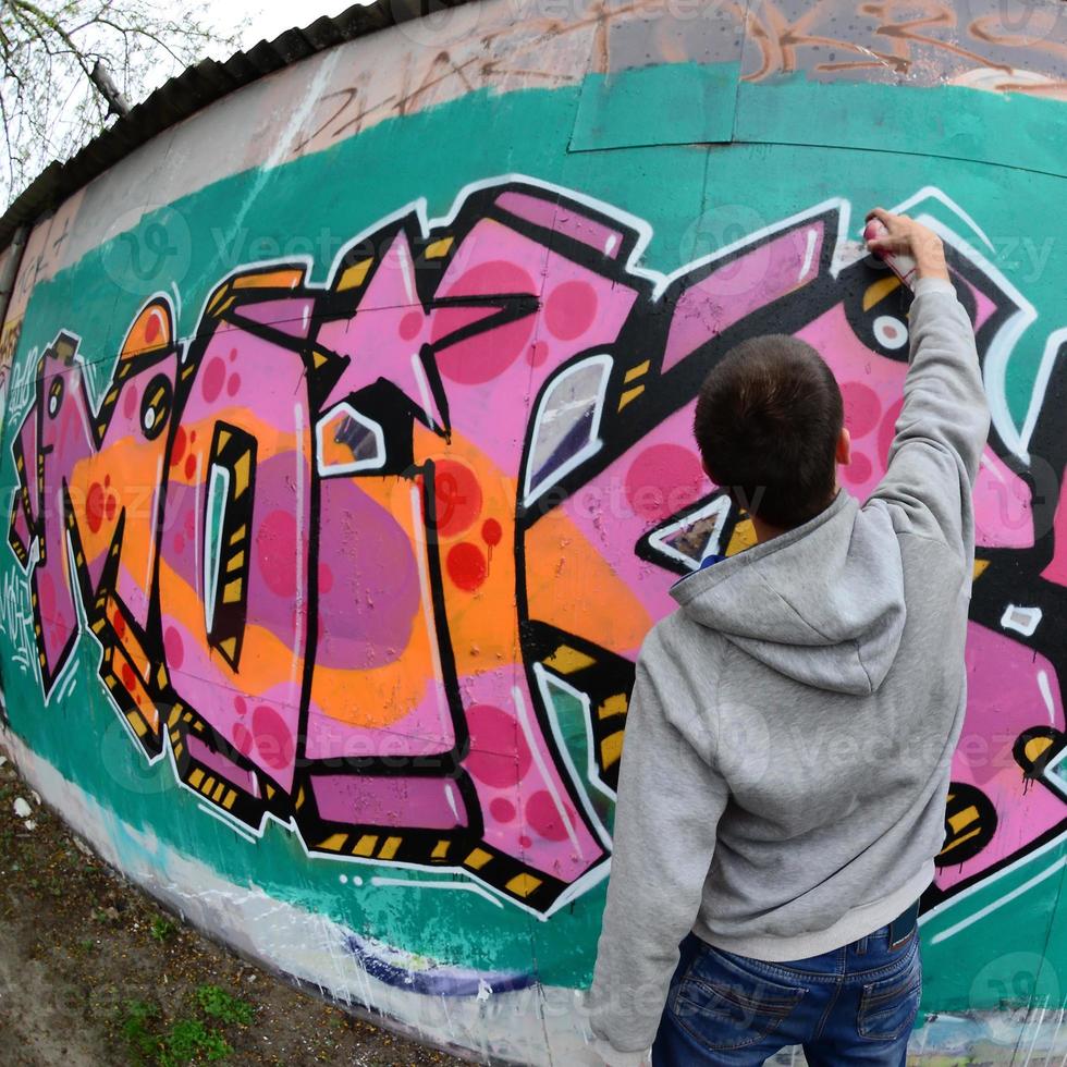 un' giovane tipo nel un' grigio felpa con cappuccio vernici graffiti nel rosa e verde c foto