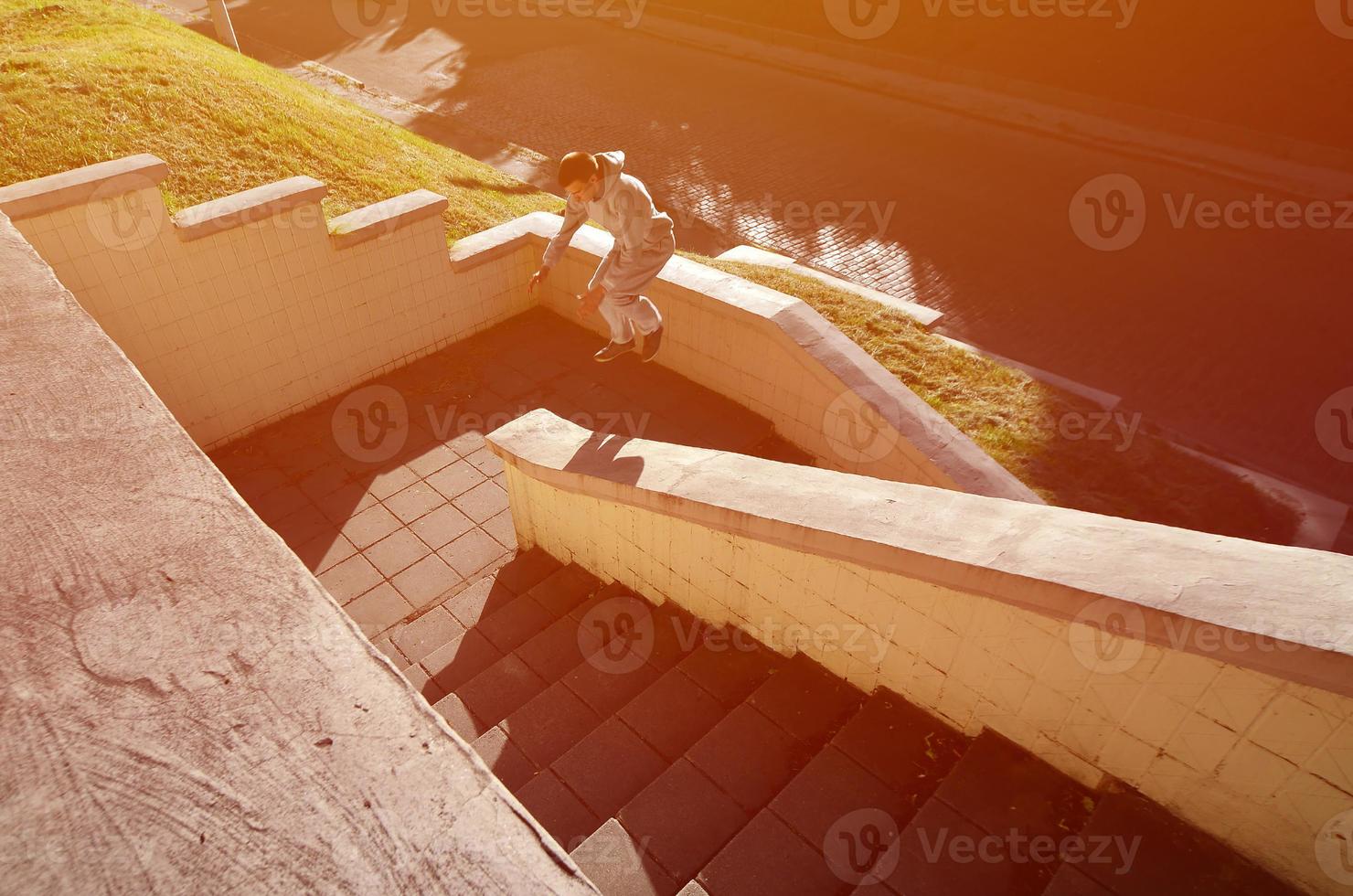 un' giovane tipo esegue un' saltare attraverso il spazio fra il calcestruzzo parapetti. il atleta pratiche parkour, formazione nel strada condizioni. il concetto di gli sport sottoculture tra gioventù foto