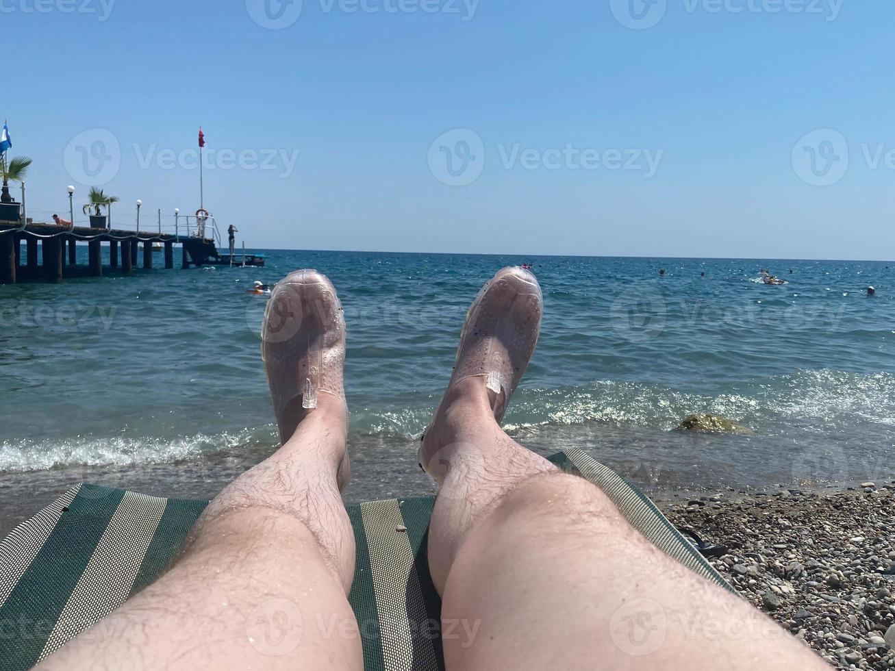 maschio peloso gambe di un' vacanziere su un' sole lettino su il spiaggia a il mare foto