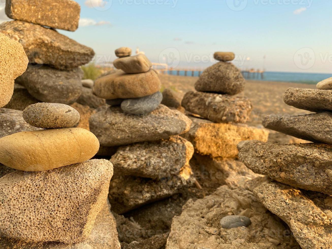 un' piramide di pietre impilati su superiore di ogni altro su il spiaggia e sabbia con piccolo naturale multicolore pietre su il riva contro il fondale di il mare a tramonto foto