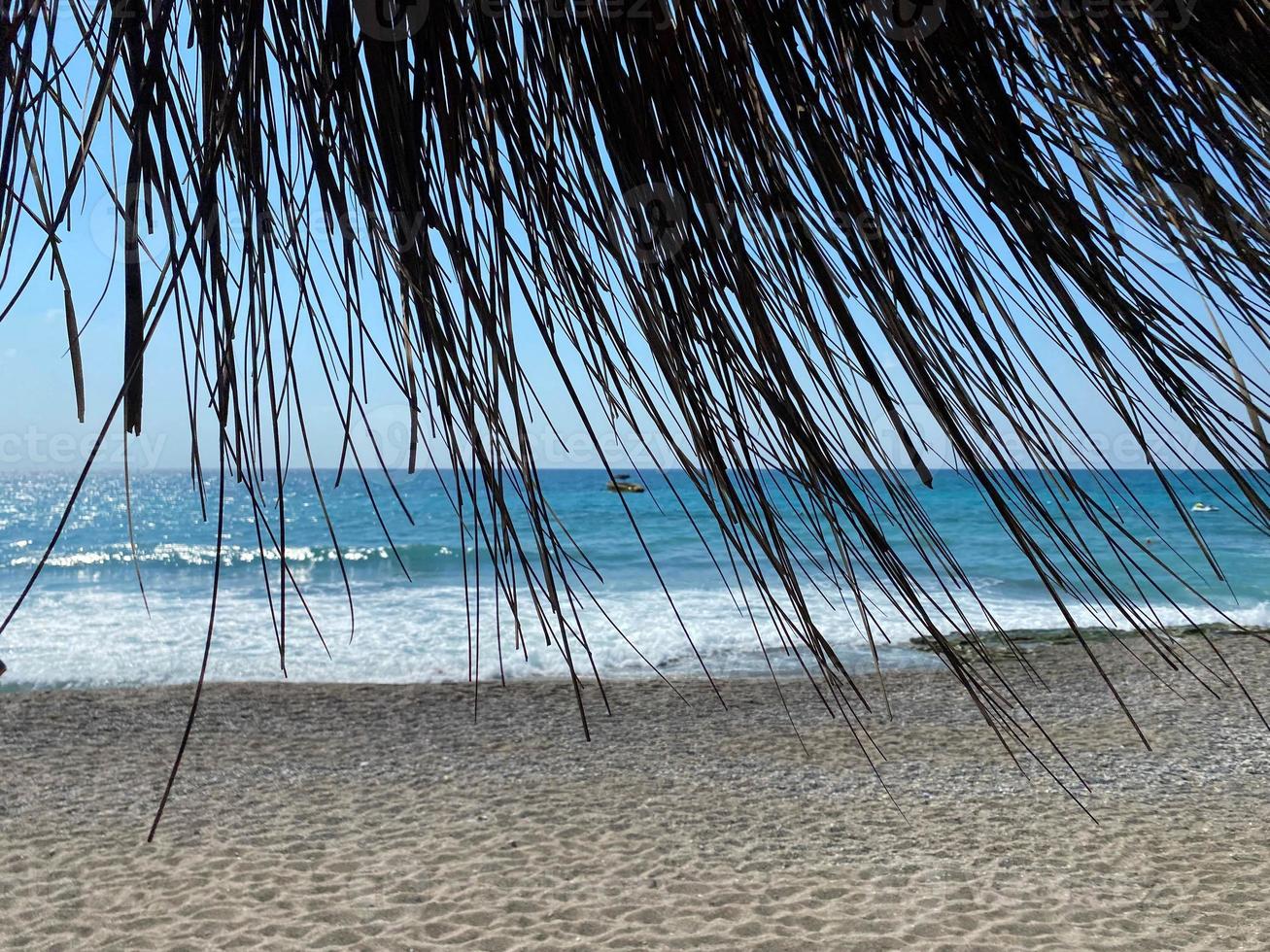 Visualizza di il blu mare con sale acqua attraverso il giallo asciutto cannuccia di il sole ombrello su il spiaggia nel il caldo orientale tropicale nazione meridionale Paradiso ricorrere. il sfondo foto