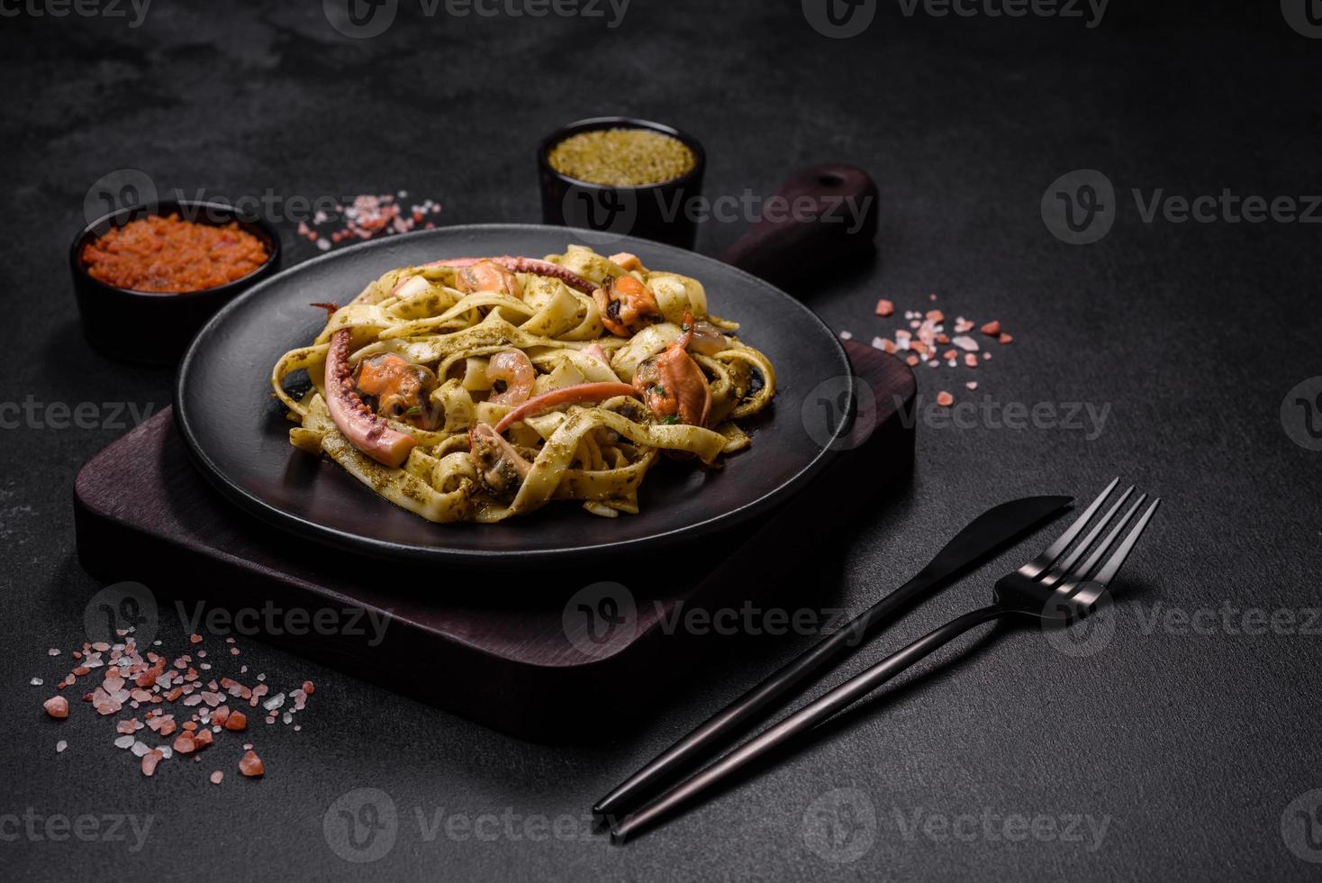 delizioso fresco pasta con pesto salsa e frutti di mare su un' nero piatto foto