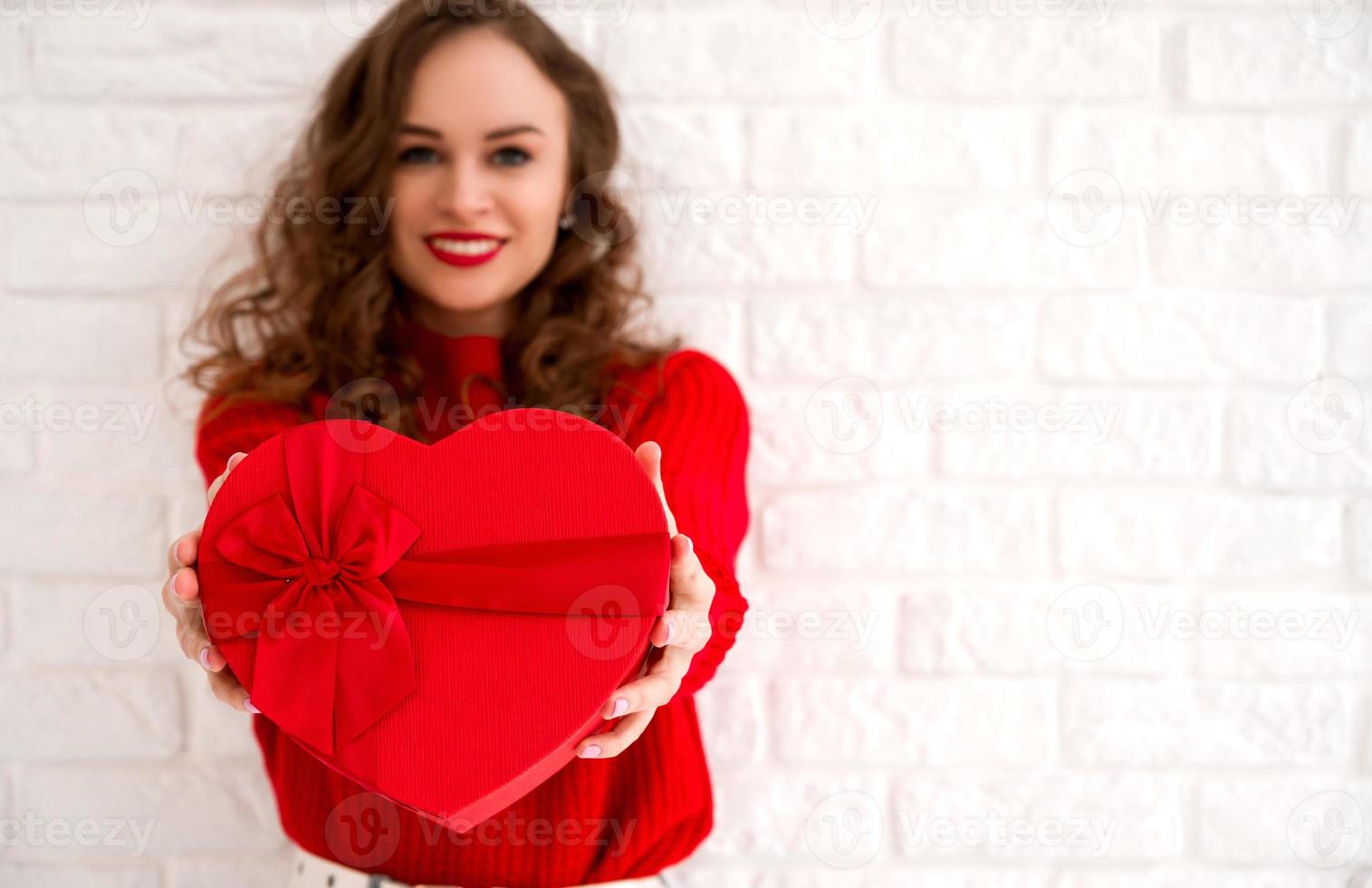 avvicinamento di un' cuore sagomato regalo con nel mani di un' yound sorridente donna. san valentino, compleanno, anniversario ecc. copyspace banner.focus su il scatola foto