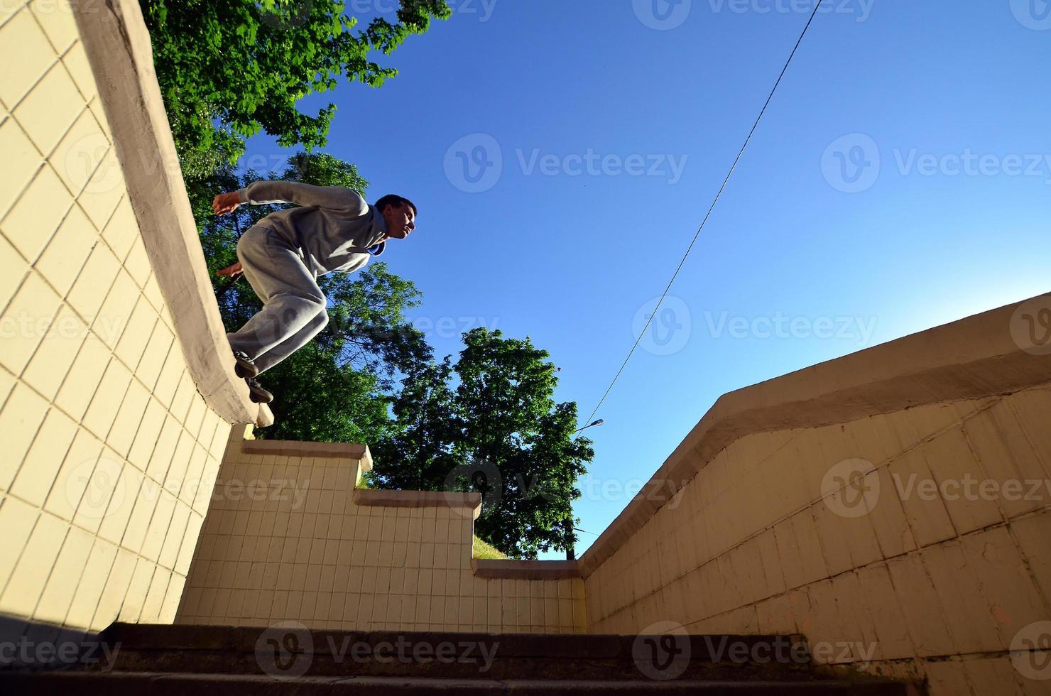 un' giovane tipo esegue un' saltare attraverso il spazio fra il calcestruzzo parapetti. il atleta pratiche parkour, formazione nel strada condizioni. parte inferiore Visualizza foto