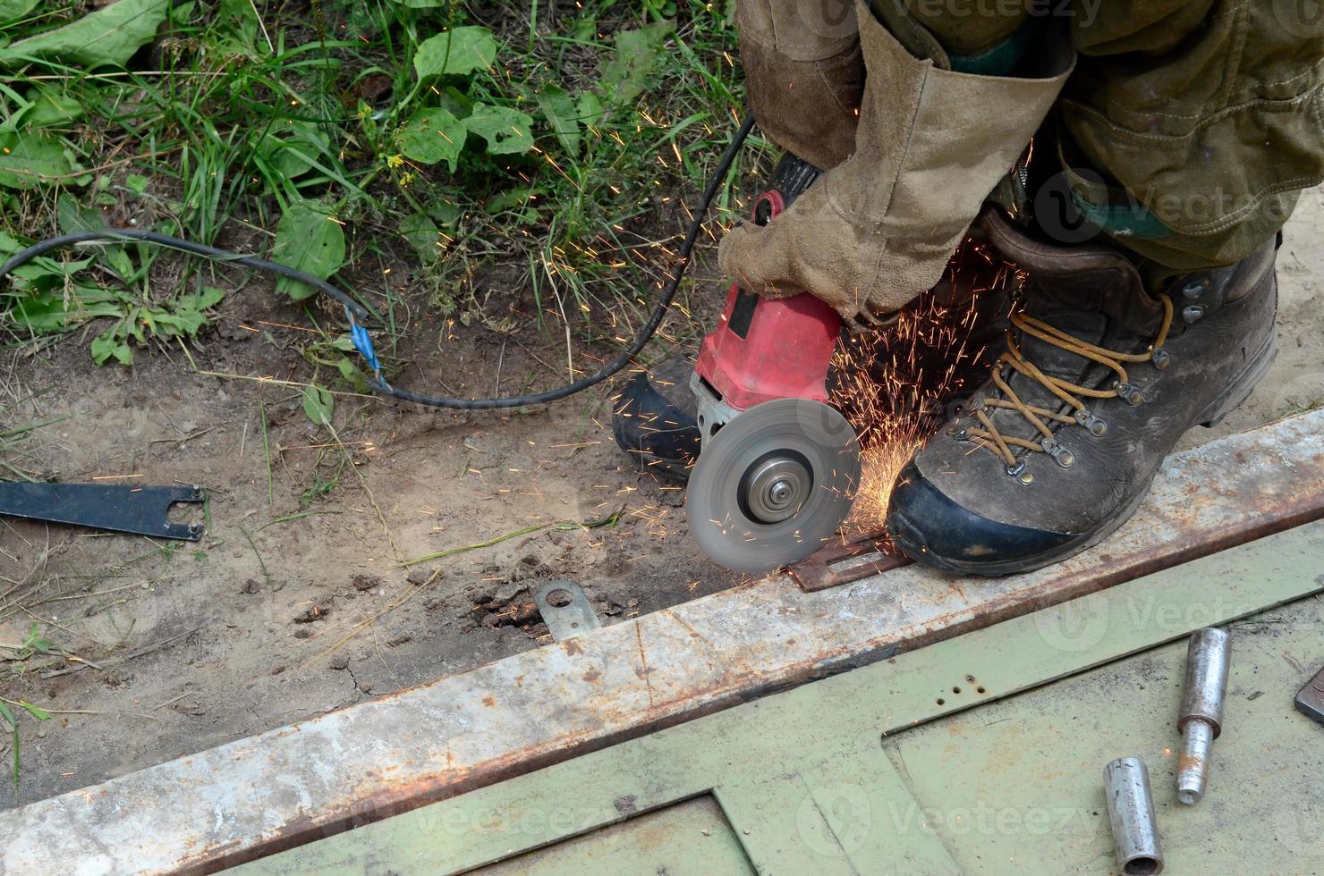 elettrico ruota macinazione su acciaio struttura all'aperto. vecchio Manuale lavoratore nel protettivo guanti taglio metallo porta con macinino foto