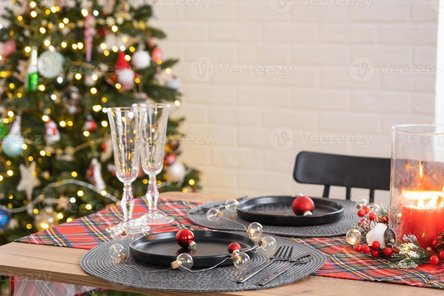 festivo tavolo impostato nel il vivente camera per Natale e nuovo anno nel soffitta stile. Natale albero, nero piatti e forchette, intrecciata tovaglioli, di moda stoviglie, accogliente interno di il Casa foto