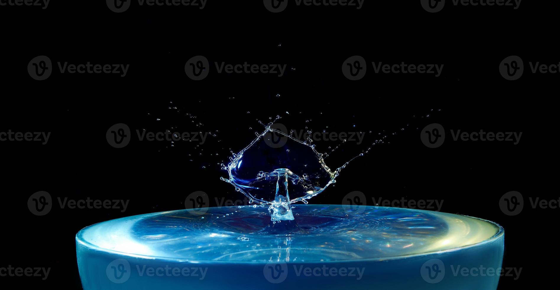 un' spruzzo di blu acqua con un' far cadere volante a partire dal sopra su un' nero sfondo foto