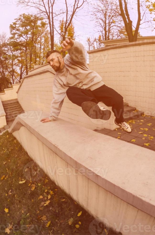 un' giovane tipo esegue un' saltare attraverso il calcestruzzo parapetto. il atleta pratiche parkour, formazione nel strada condizioni. il concetto di gli sport sottoculture tra gioventù foto