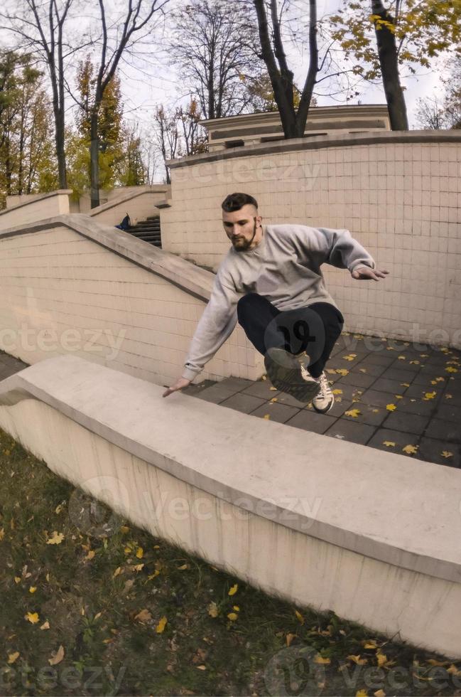 un' giovane tipo esegue un' saltare attraverso il calcestruzzo parapetto. il atleta pratiche parkour, formazione nel strada condizioni. il concetto di gli sport sottoculture tra gioventù foto