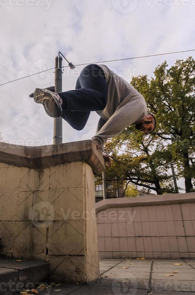 un' giovane tipo esegue un' saltare attraverso il calcestruzzo parapetto. il atleta pratiche parkour, formazione nel strada condizioni. il concetto di gli sport sottoculture tra gioventù foto