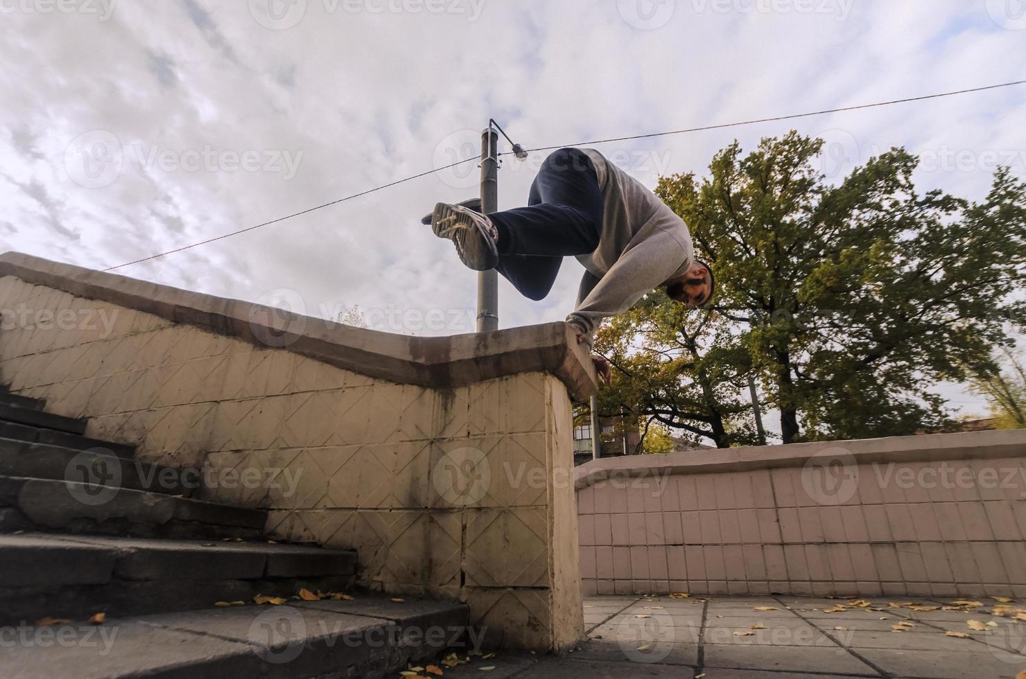 un' giovane tipo esegue un' saltare attraverso il calcestruzzo parapetto. il atleta pratiche parkour, formazione nel strada condizioni. il concetto di gli sport sottoculture tra gioventù foto