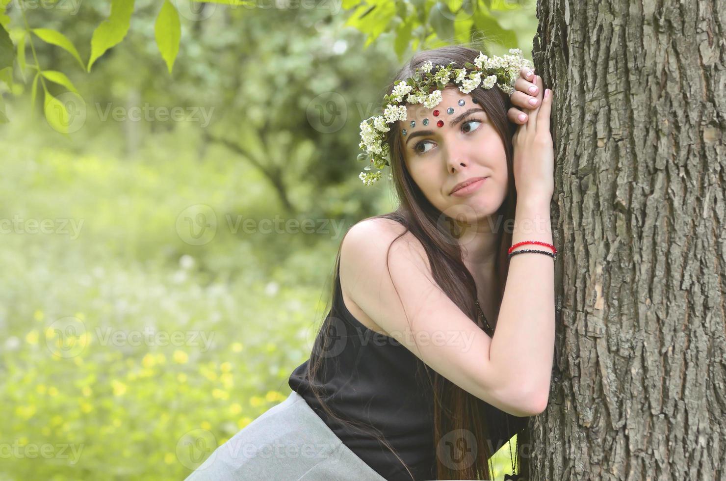 un' foresta immagine di un' bellissimo giovane brunetta di europeo aspetto con buio Marrone occhi e grande labbra. su il ragazze testa è indossare un' floreale ghirlanda, su sua fronte brillante decorazioni foto