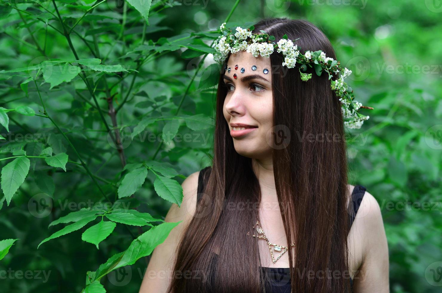 un' foresta immagine di un' bellissimo giovane brunetta di europeo aspetto con buio Marrone occhi e grande labbra. su il ragazze testa è indossare un' floreale ghirlanda, su sua fronte brillante decorazioni foto