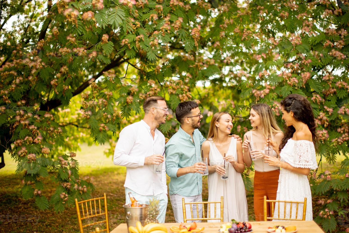 gruppo di contento giovane persone applauso con fresco limonata e mangiare frutta nel il giardino foto