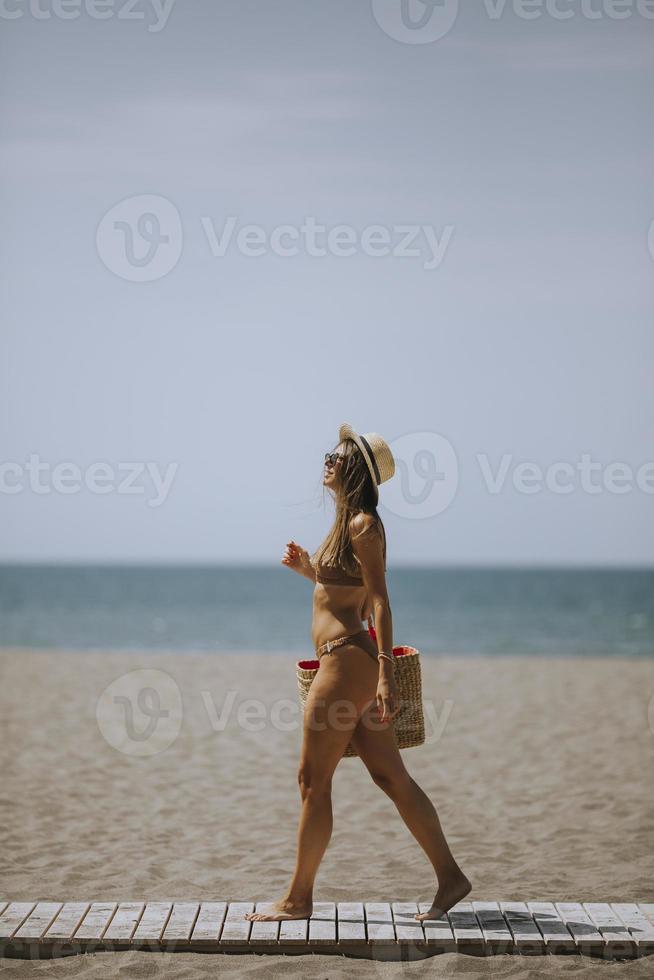 giovane donna nel bikini con cannuccia Borsa su il spiaggia a estate giorno foto