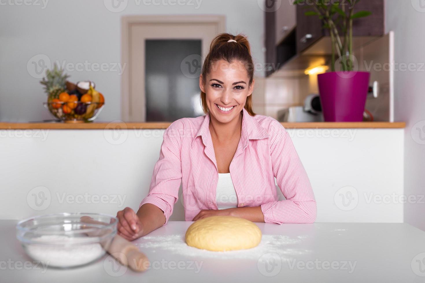 bellissimo giovane donna guardare a telecamera e sorridente mentre cottura al forno nel cucina a casa. sorridente giovane casalinga fabbricazione Impasto foto