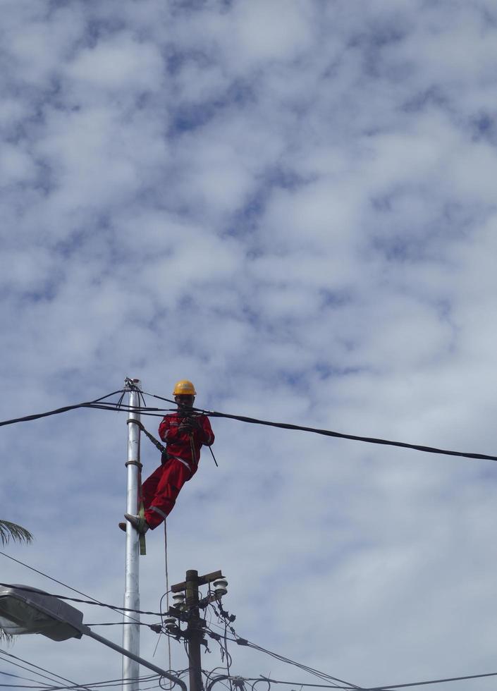 gorontalo-indonesia, dicembre 2022 - tecnici Collegare cavi per elettrico poli. dipendente sospeso di cintura su elettricità polo per posa Basso voltaggio cavo foto