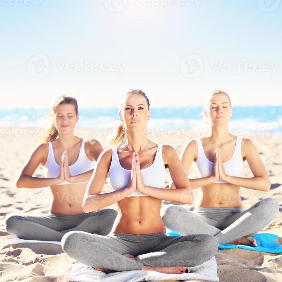 gruppo di donne praticando yoga su il spiaggia foto