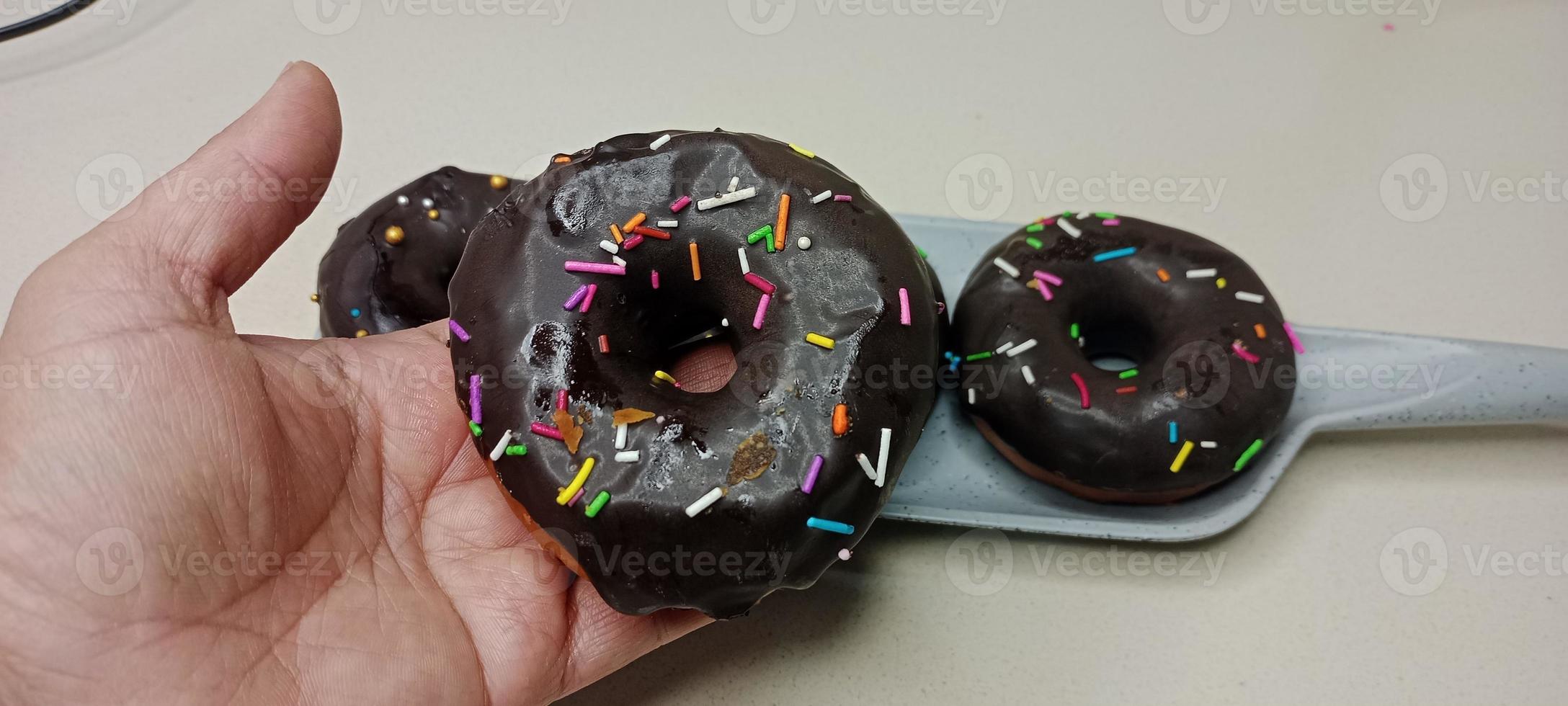 assortito ciambelle con cioccolato glassato, rosa smaltato e spruzzatori ciambelle. ciambelle nel mano o vassoio foto