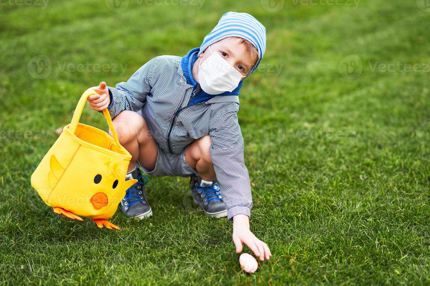 poco ragazzo indossare protettivo maschera a caccia per Pasqua uovo nel primavera giardino. foto