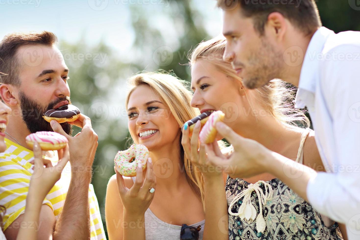 gruppo di amici mangiare ciambelle all'aperto foto