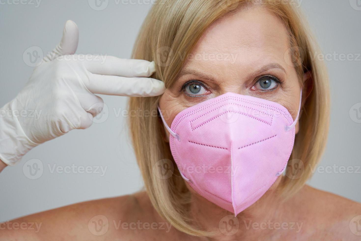 anziano donna nel rosa maschera in posa al di sopra di grigio sfondo foto