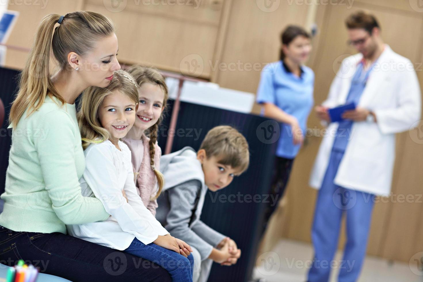 madre e bambini in attesa nel davanti di registrazione scrivania nel ospedale foto