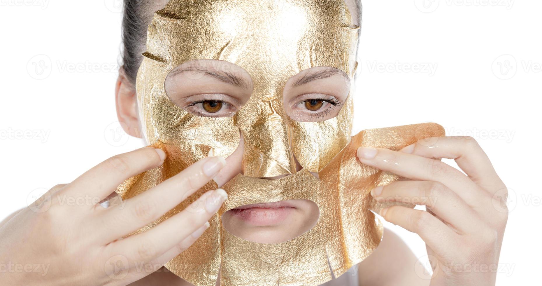 cosmetico procedura, il donna di viso con oro maschera su bianca sfondo foto