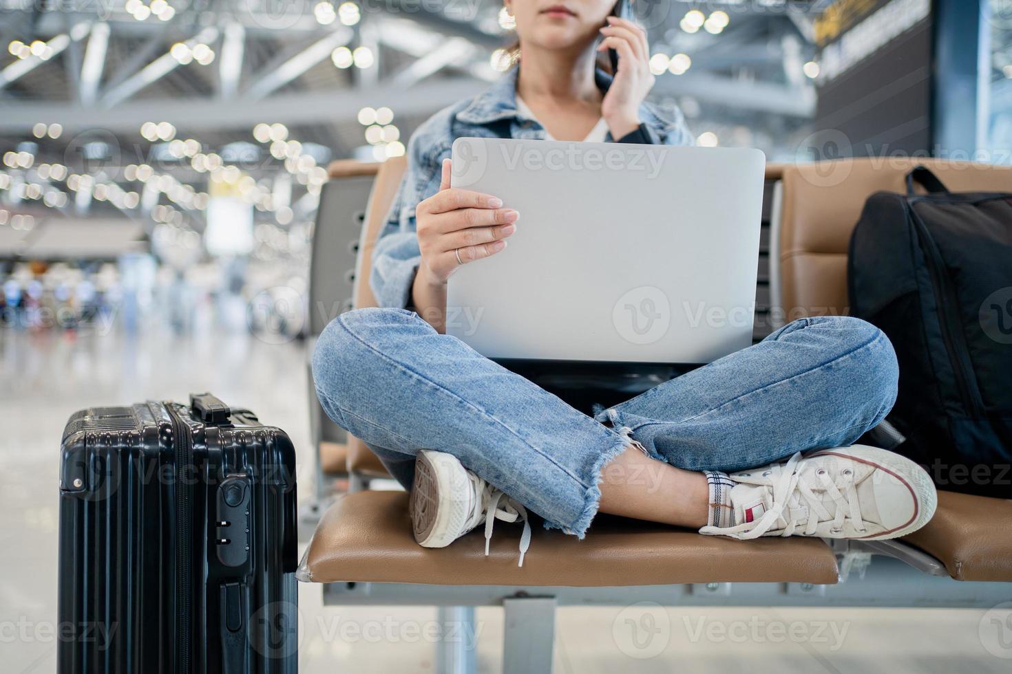 viaggio vacanza concetto, asiatico femmina donna usi un' smartphone e è Lavorando su un' computer portatile, lei sedersi wating per volo programma a terminale aeroporto. foto