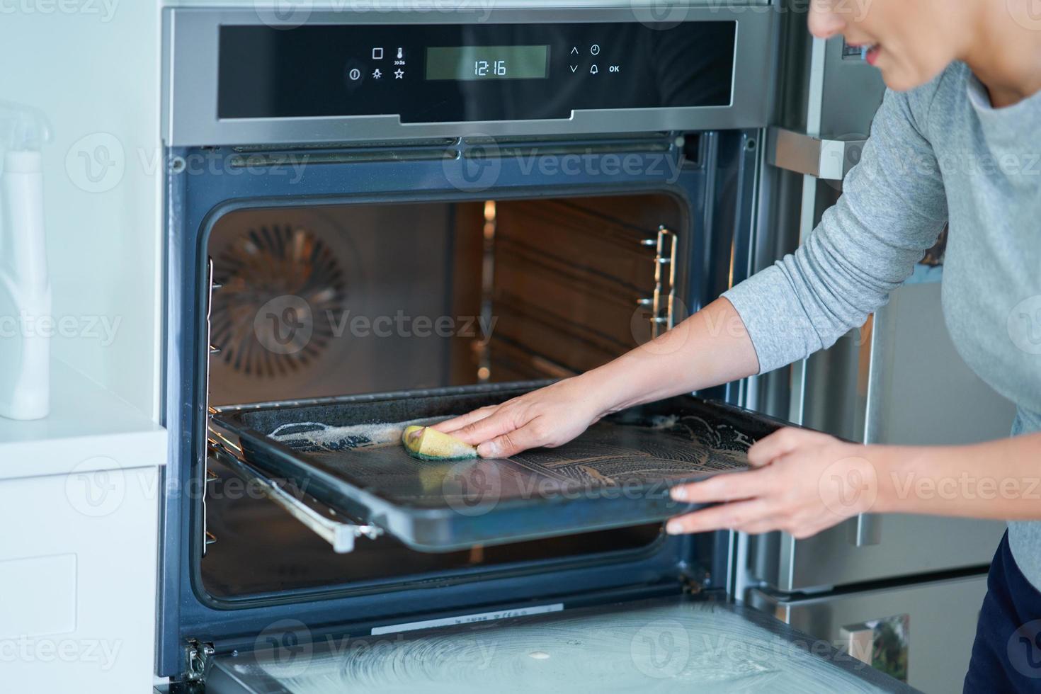 giovane donna pulizia forno nel il cucina foto